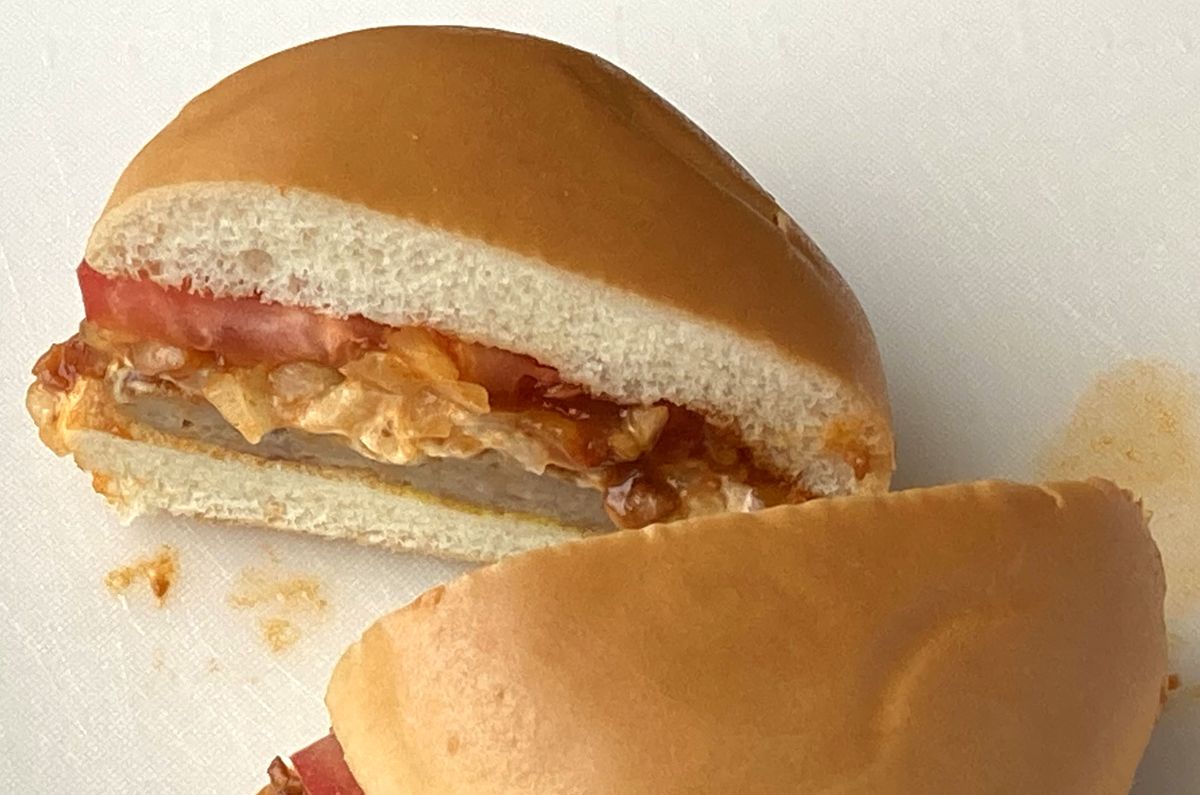 半分に切ったモスバーガーの断面。上のバンズの下に輪切りのトマト、その下に玉ねぎ入りのミートソースとパティ、下のバンズが重なっている。